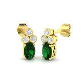 Gold stud earrings featuring oval emerald and three round bezel set diamonds