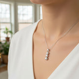 white gold necklace with a pendant worn by a person in a blurred indoor setting