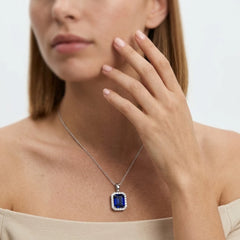 FineDiam deep blue emerald cut gemstone pendant framed by small round diamonds in a white metal setting.