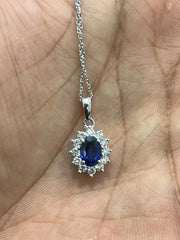 FineDiam oval dark blue gemstone pendant with a sparkling white stone halo and polished white metal setting.