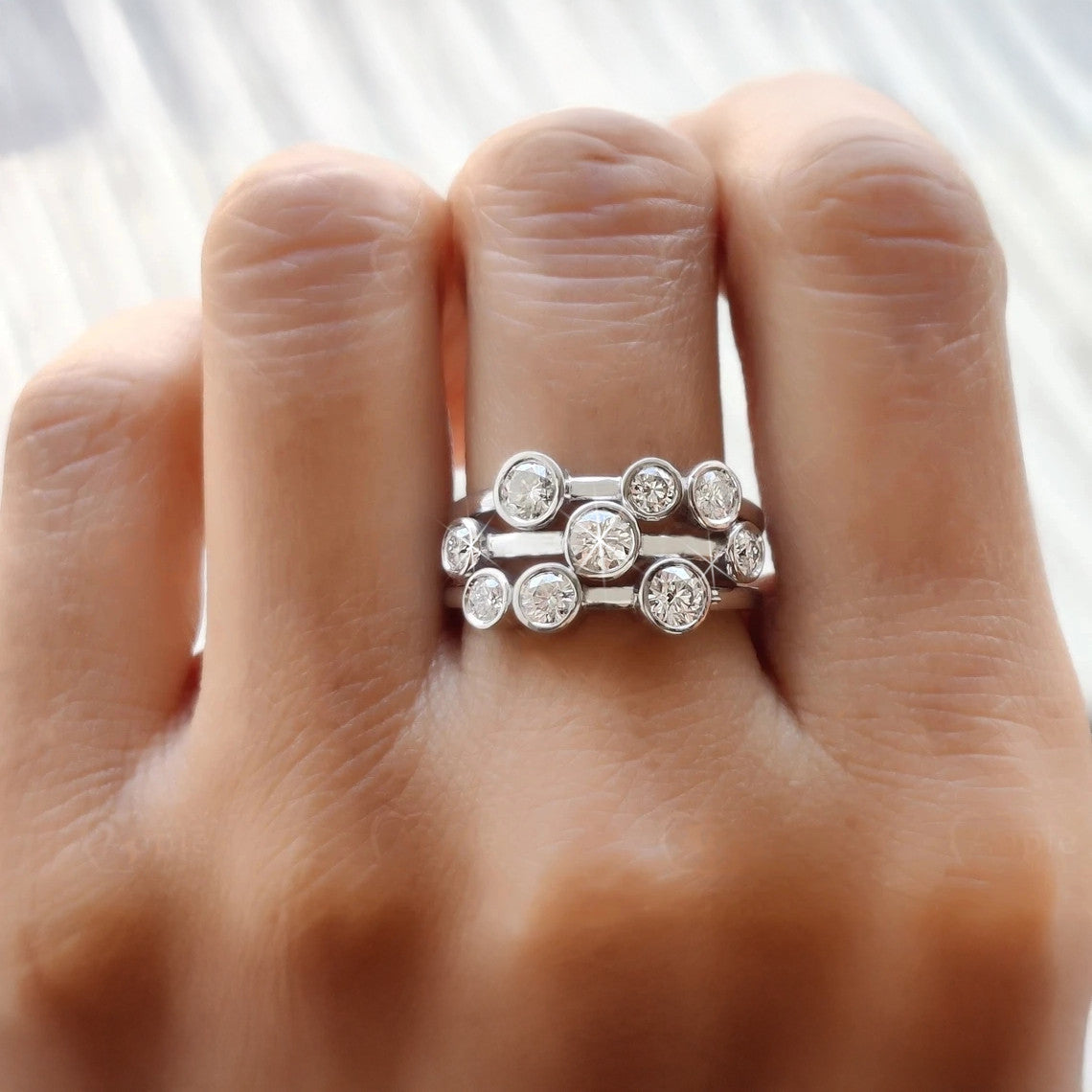 Silver ring with multiple diamonds on a person's finger against a neutral background