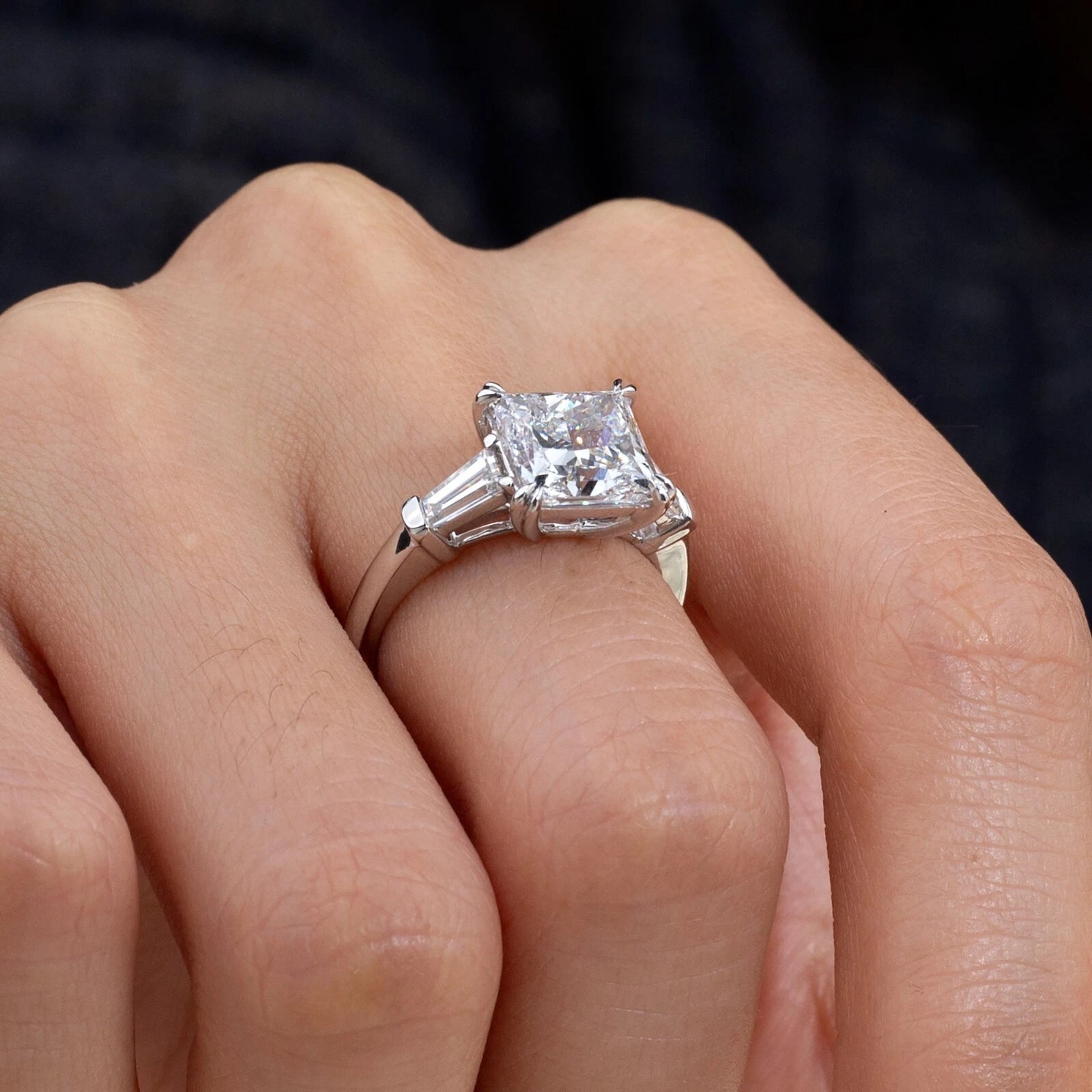 Silver ring with a large diamond on a person's finger against a dark background