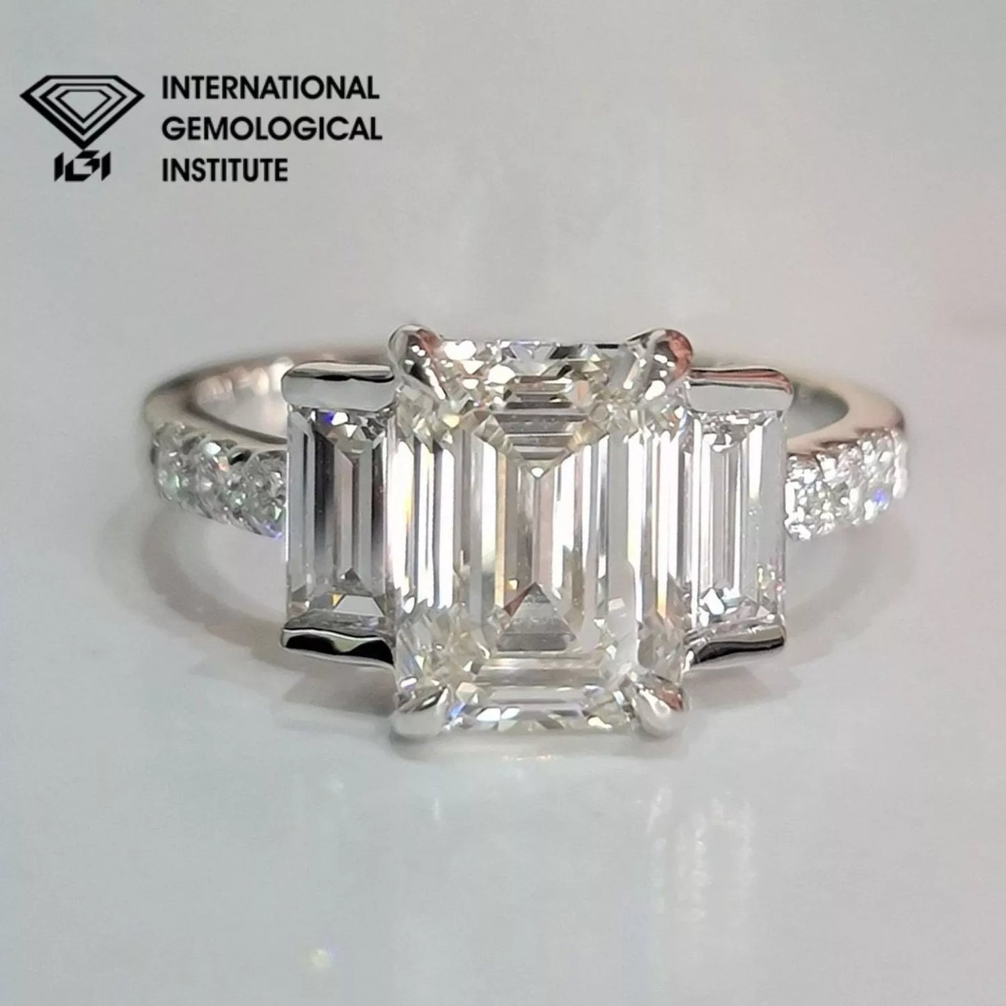 Diamond ring with emerald-cut diamonds on a gray background, featuring the International Gemological Institute logo.