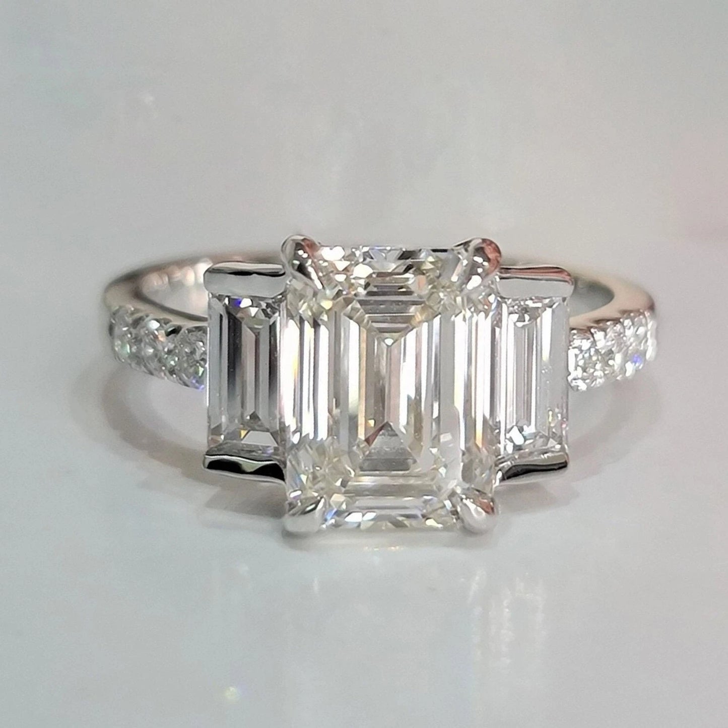 Diamond ring with emerald-cut stones on a light gray background