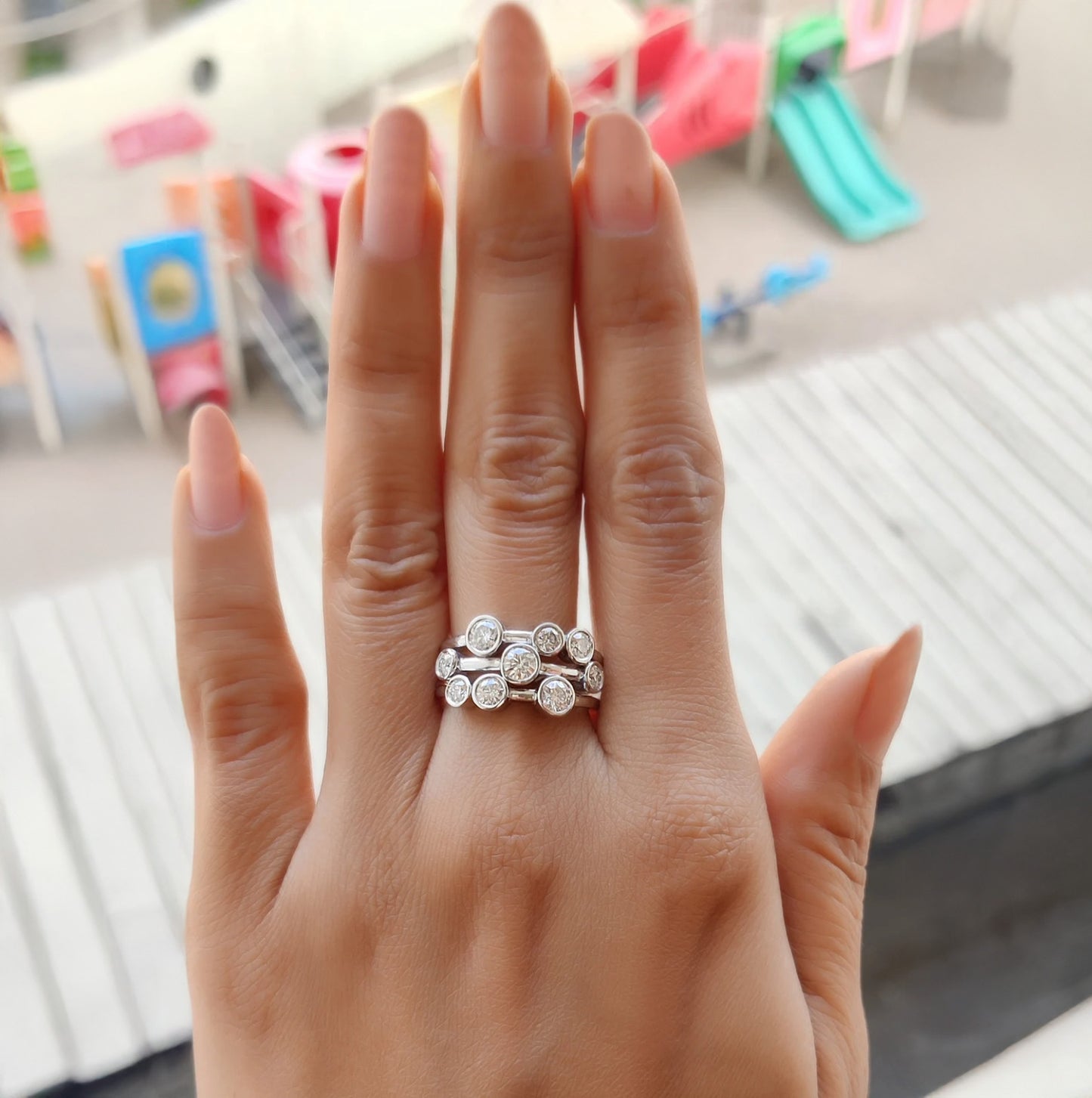 Hand wearing a silver ring with a blurred background of colorful playground equipment