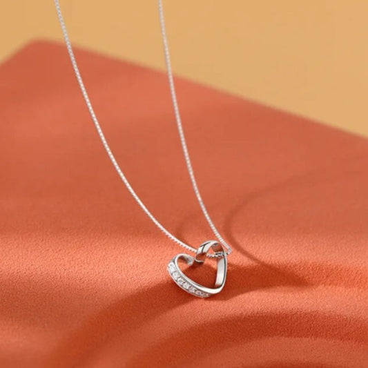 A white gold heart-shaped pendant necklace with a diamond chain displayed on a orange surface.