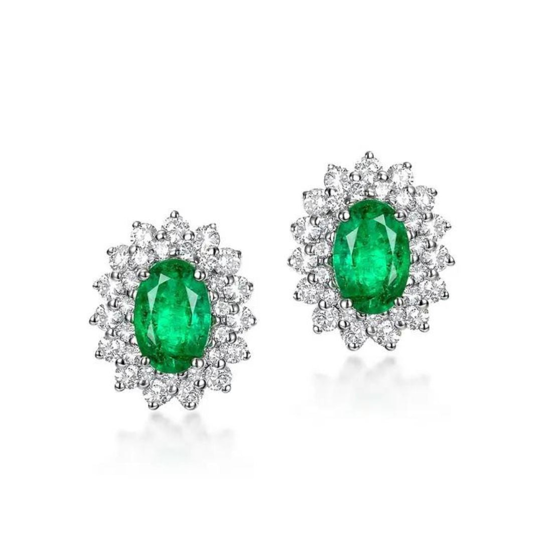 A pair of 18K white gold cluster stud earrings featuring oval-shaped lab-grown diamond emeralds surrounded by smaller lab-grown diamond accents, set in a claw-type setting.