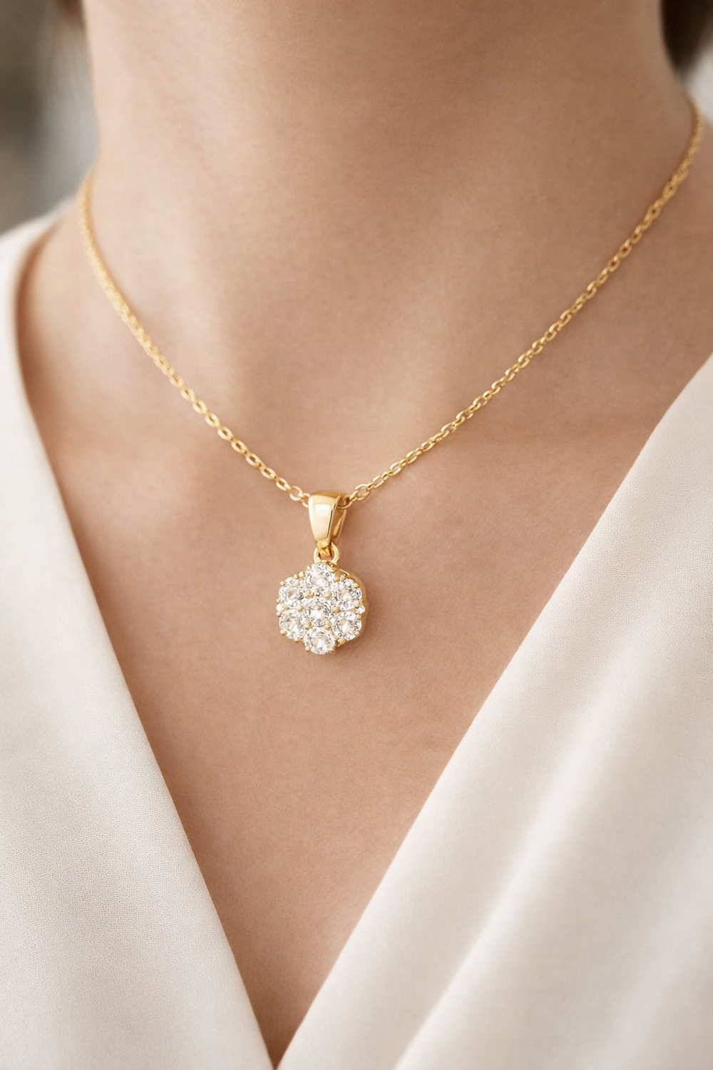 Gold necklace with a diamond pendant worn by a person in a white outfit.