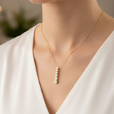 Gold necklace with a pendant on a person wearing a white top.