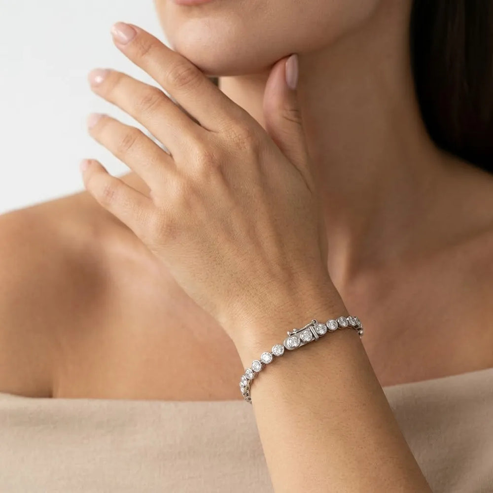 Round diamond bezel-set tennis bracelet worn on a wrist with a polished white metal clasp.