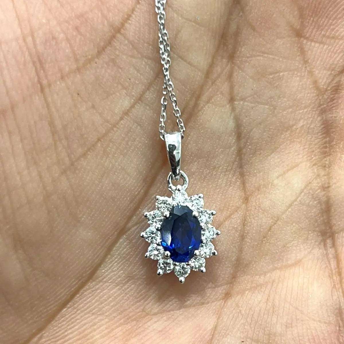 FineDiam oval blue gemstone pendant surrounded by sparkling clear stones in a decorative white metal halo.