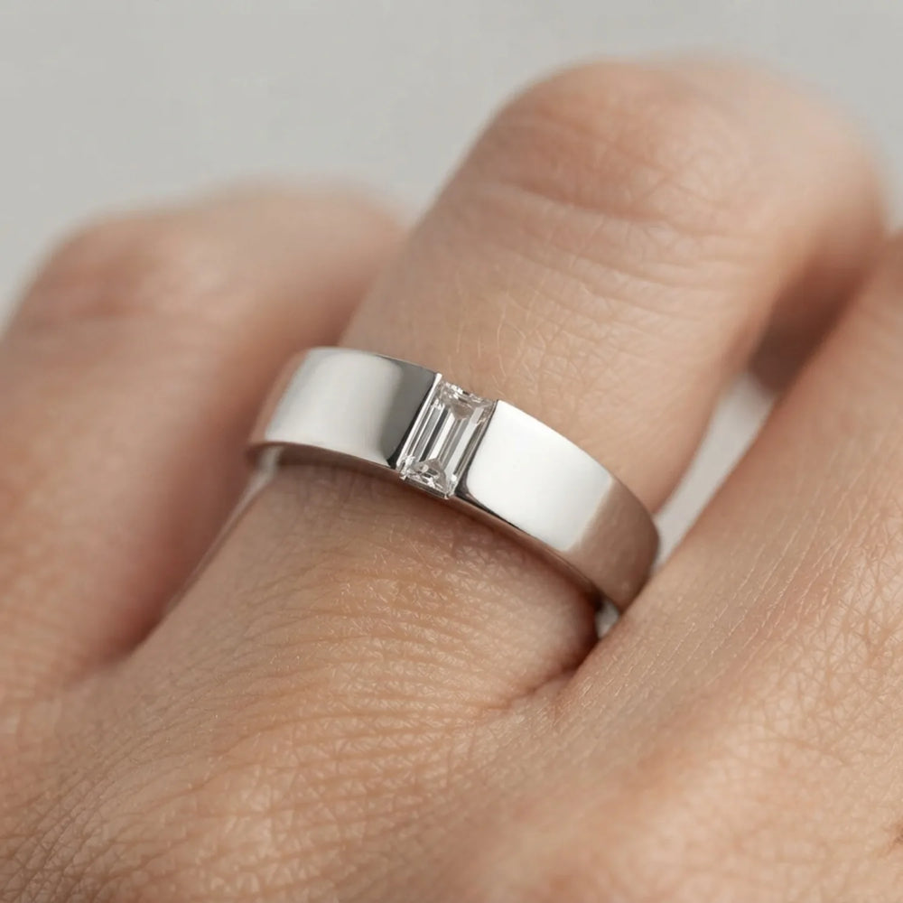 Close-up of a polished white metal band with a single baguette-cut diamond.