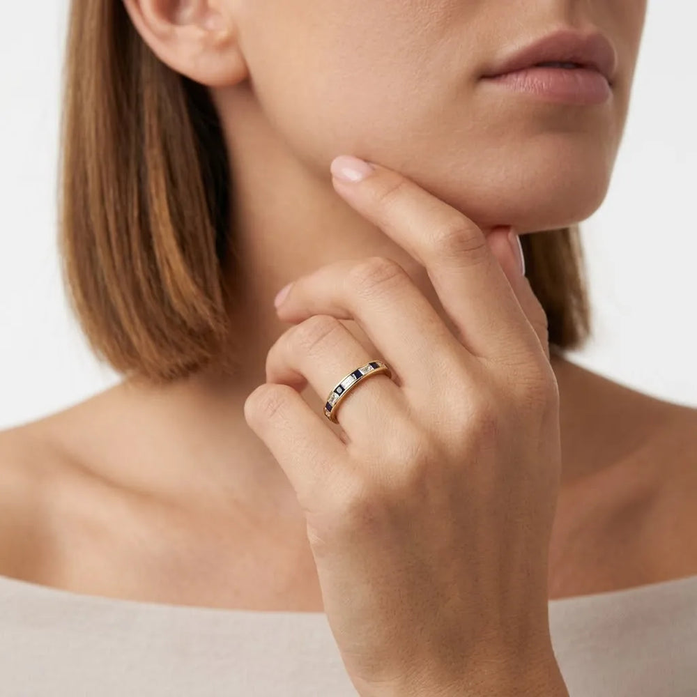 Close-up of gold band set with dark blue square gemstones and small white diamonds.