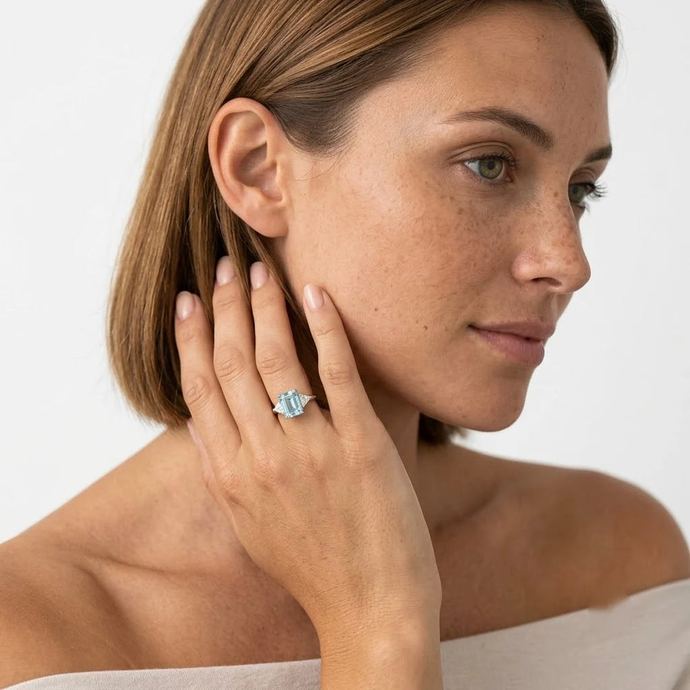  FineDiam three stone ring featuring an emerald cut light blue gemstone with triangular side stones in white metal.