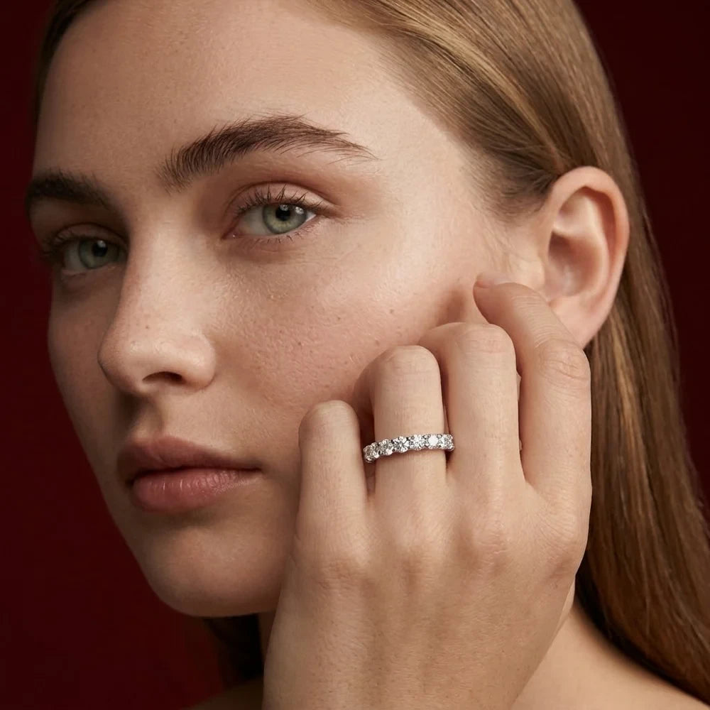FineDiam white metal ring with round diamonds, close-up view on a model's hand beside her face.