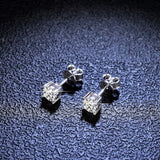 Pair of silver stud earrings with clear gemstones on a textured dark surface