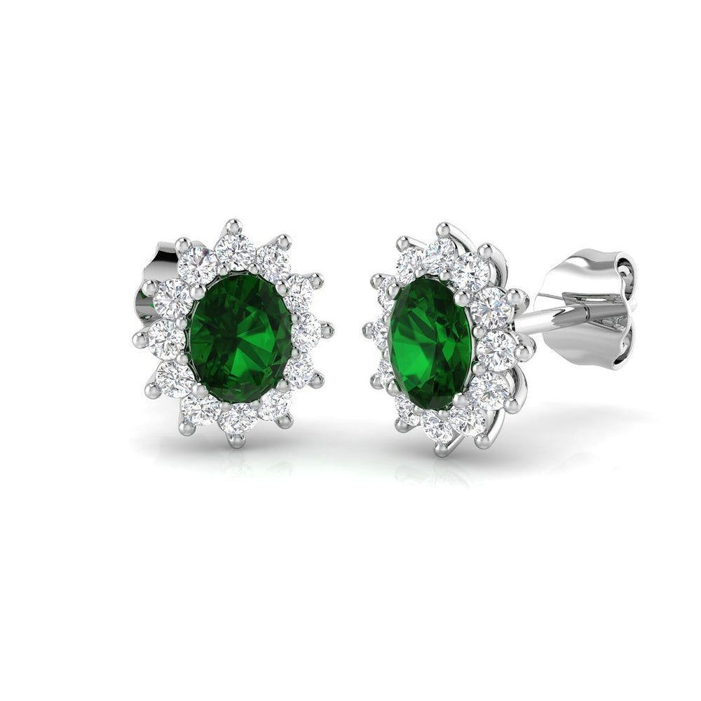 Halo stud earrings with oval emerald prong setting and cluster prong set diamonds