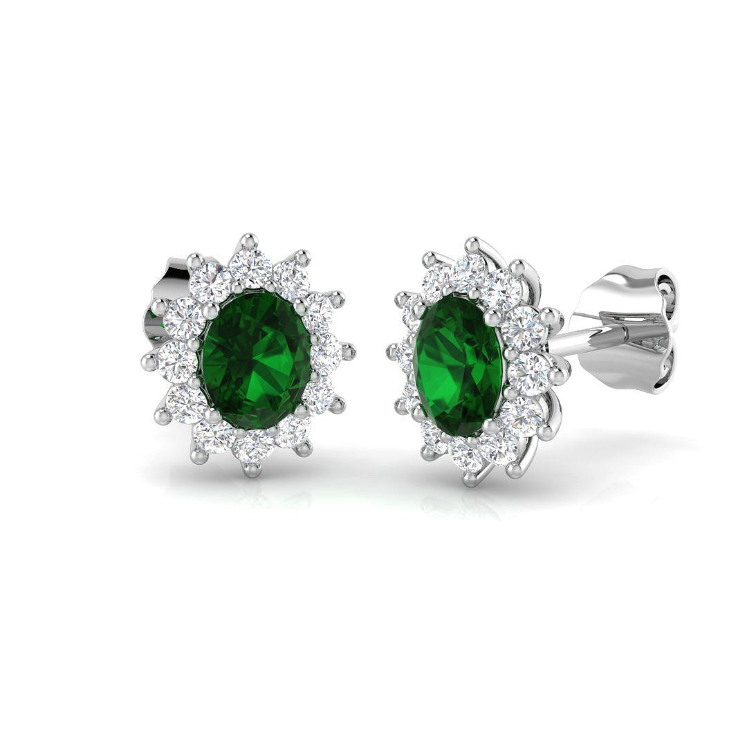 Halo stud earrings with oval emerald prong setting and cluster prong set diamonds
