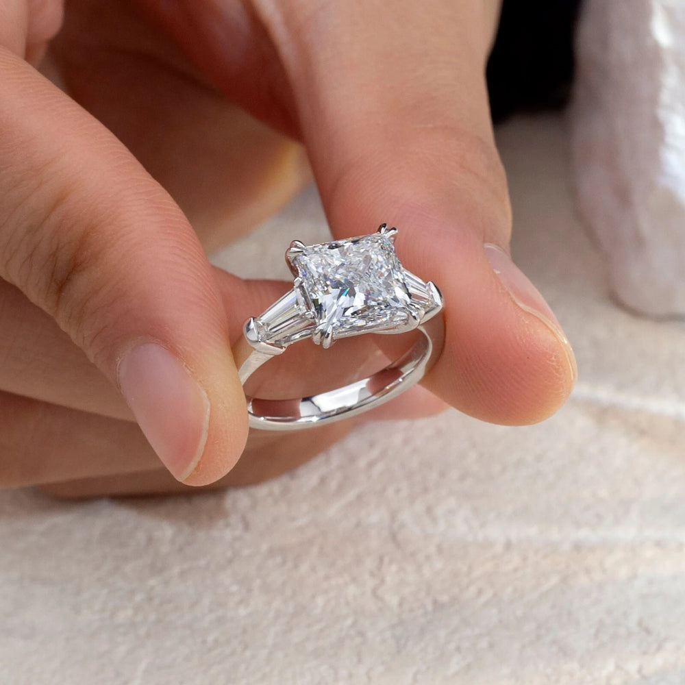 Diamond ring held between fingers on a neutral background