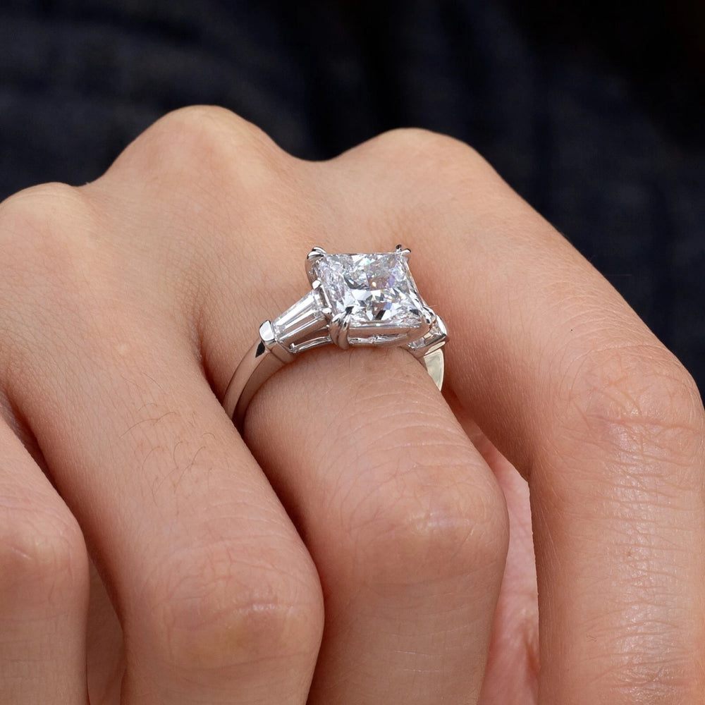 Silver ring with a large diamond on a person's finger against a dark background