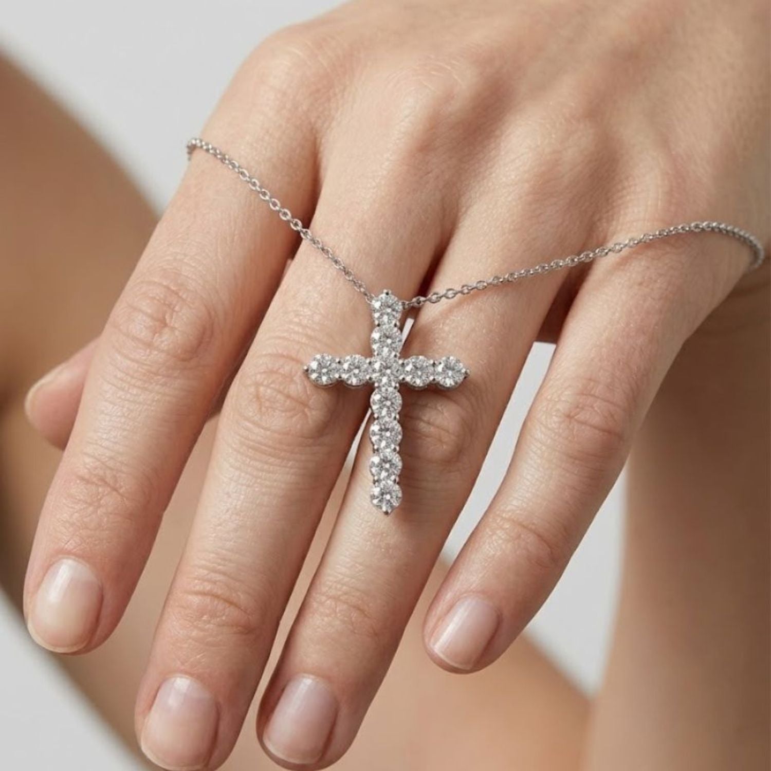 Close-up view of a hand holding a sparkling white gold cross pendant necklace set with clear round diamonds.