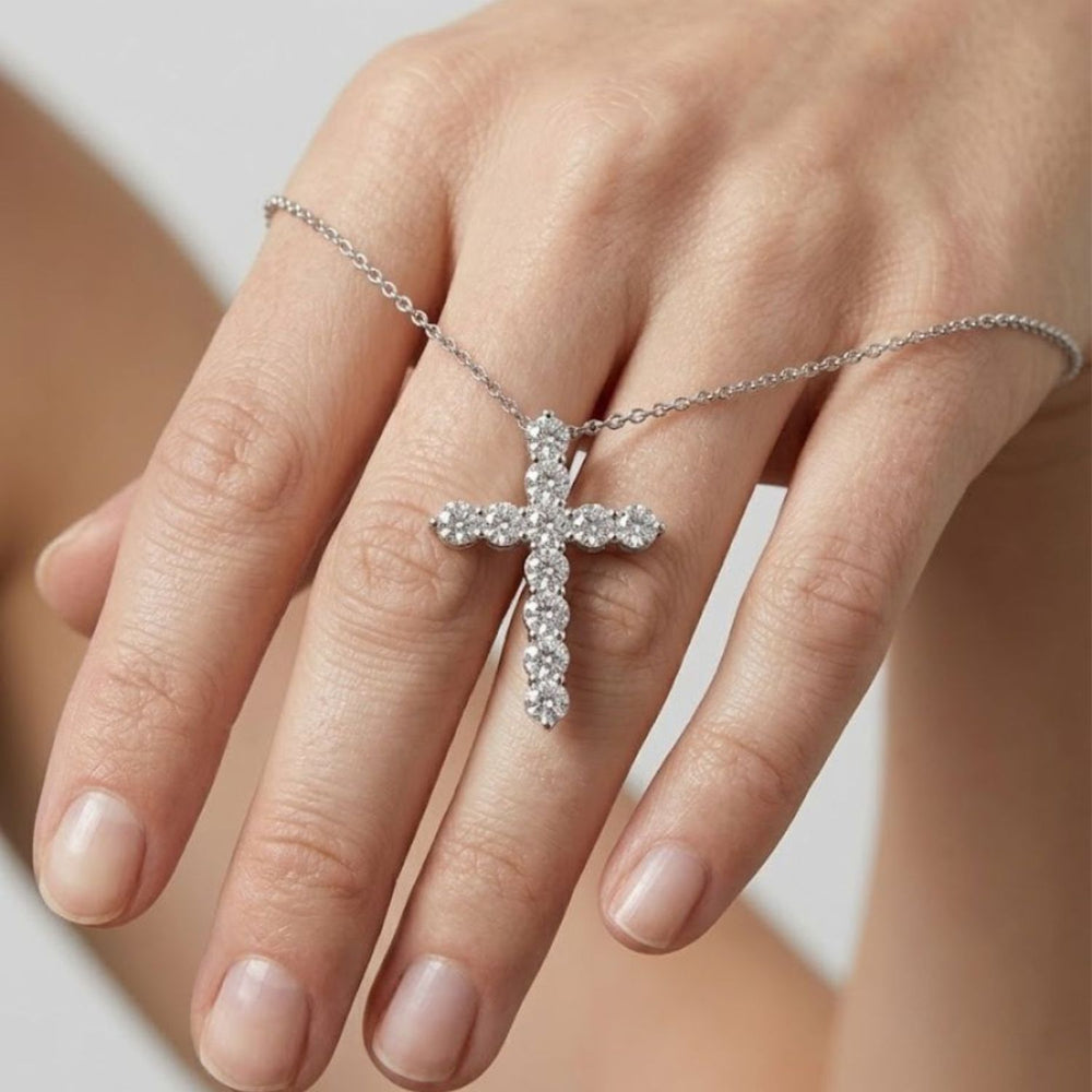 Close-up view of a hand holding a sparkling white gold cross pendant necklace set with clear round diamonds.
