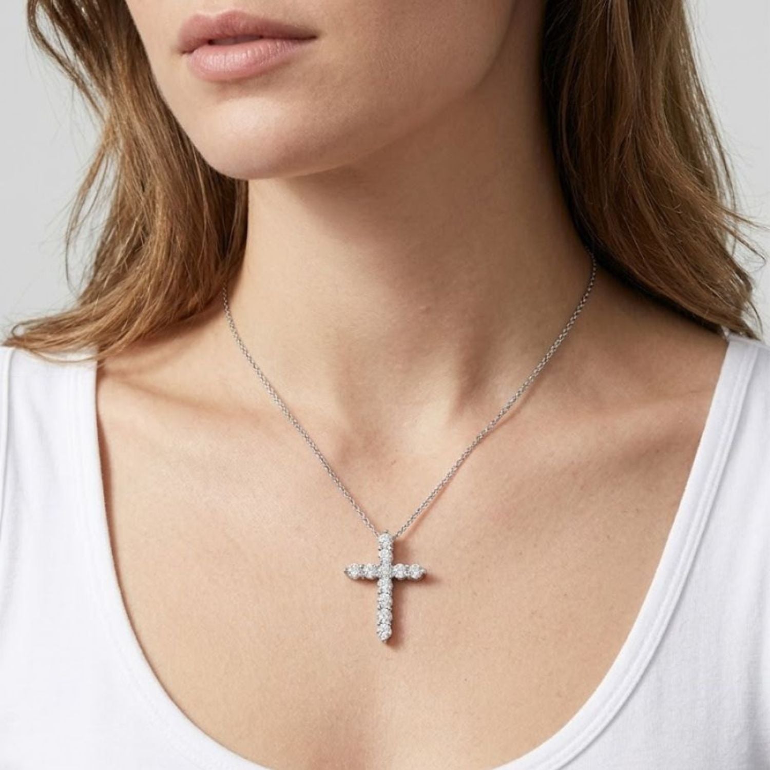 Close-up view of a woman wearing a white gold cross pendant necklace adorned with round diamonds.