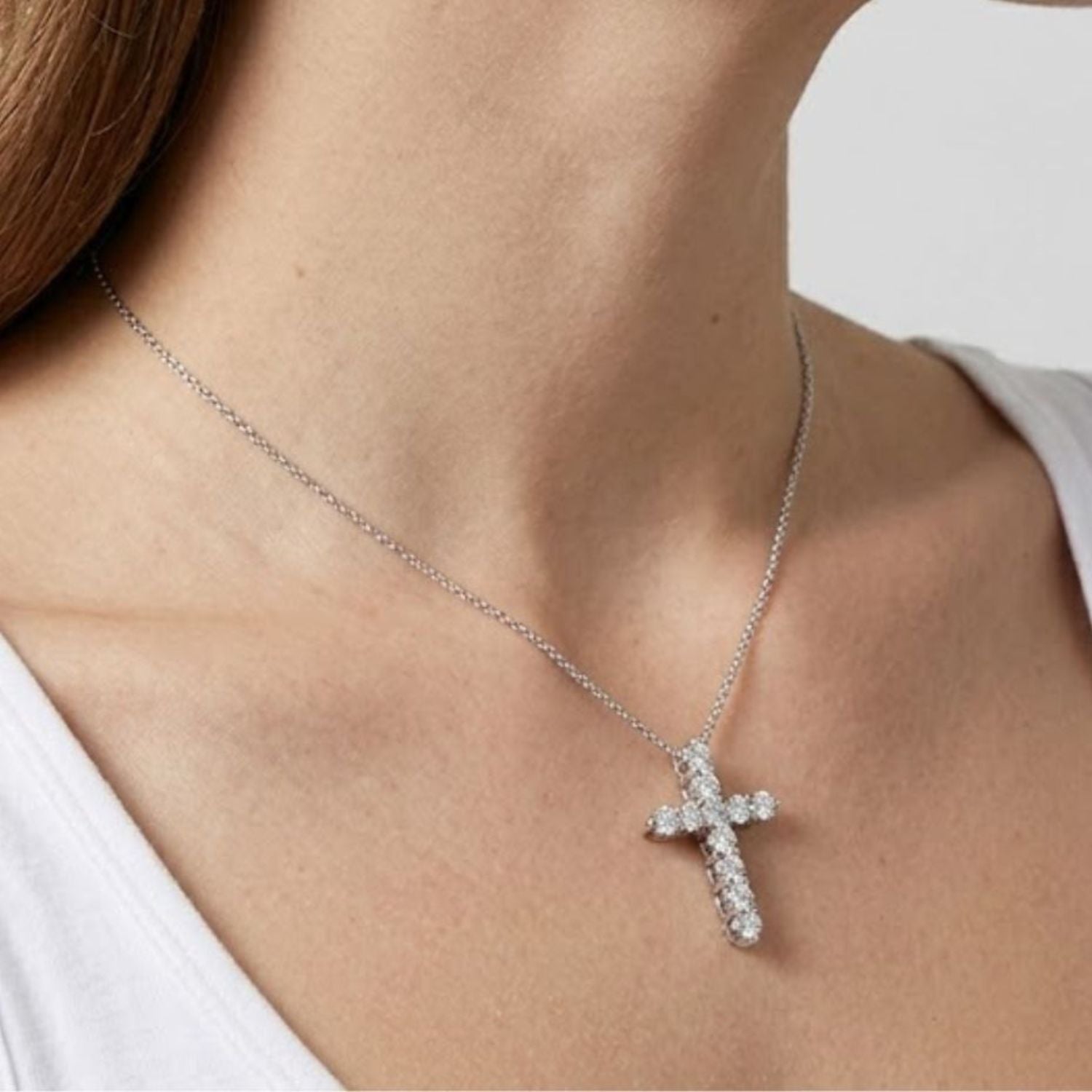 Side angle view of a woman wearing a white gold diamond cross pendant necklace with a fine chain.