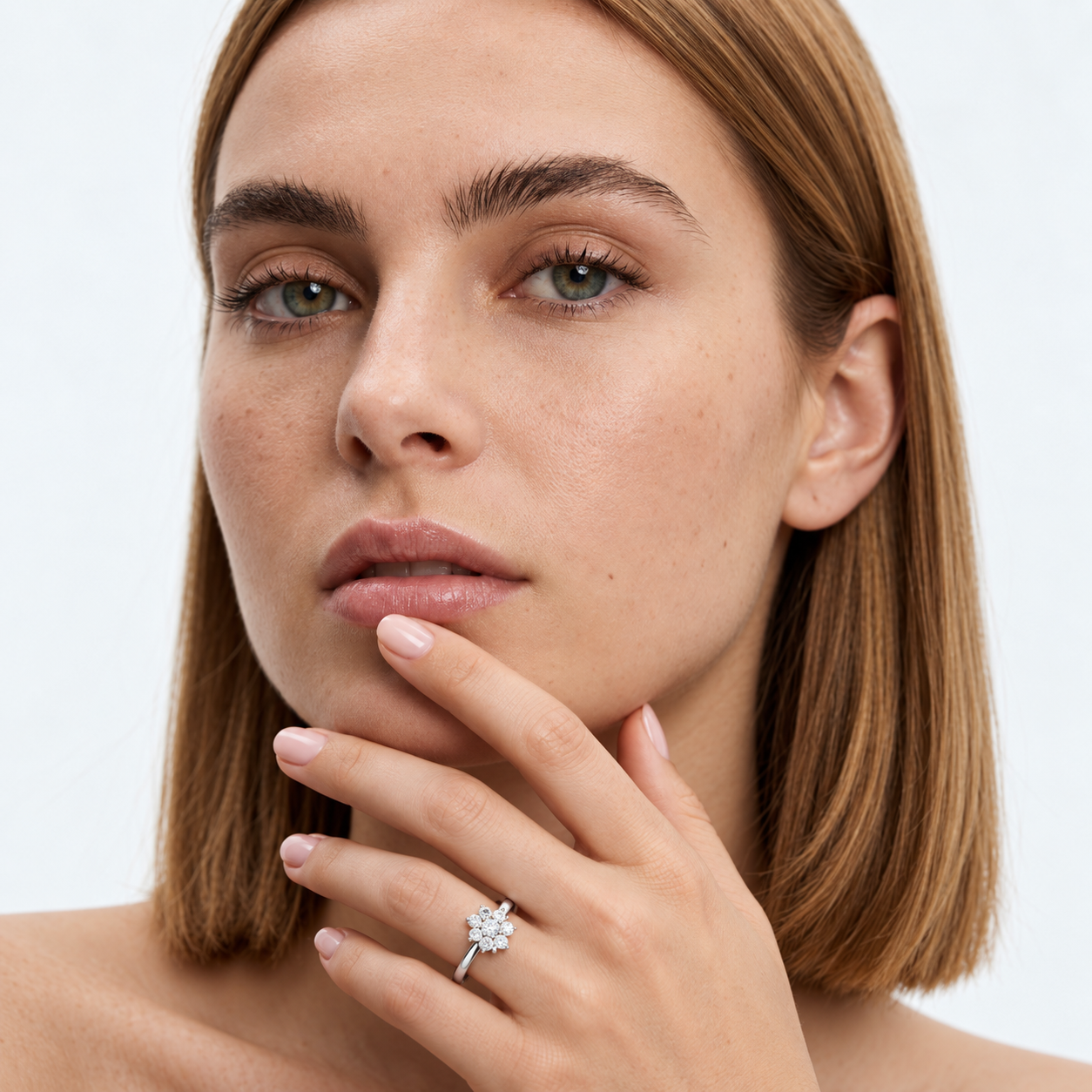 Close-up face portrait of a woman with short brown hair posing with her hand under her chin, wearing a white gold floral cluster ring.